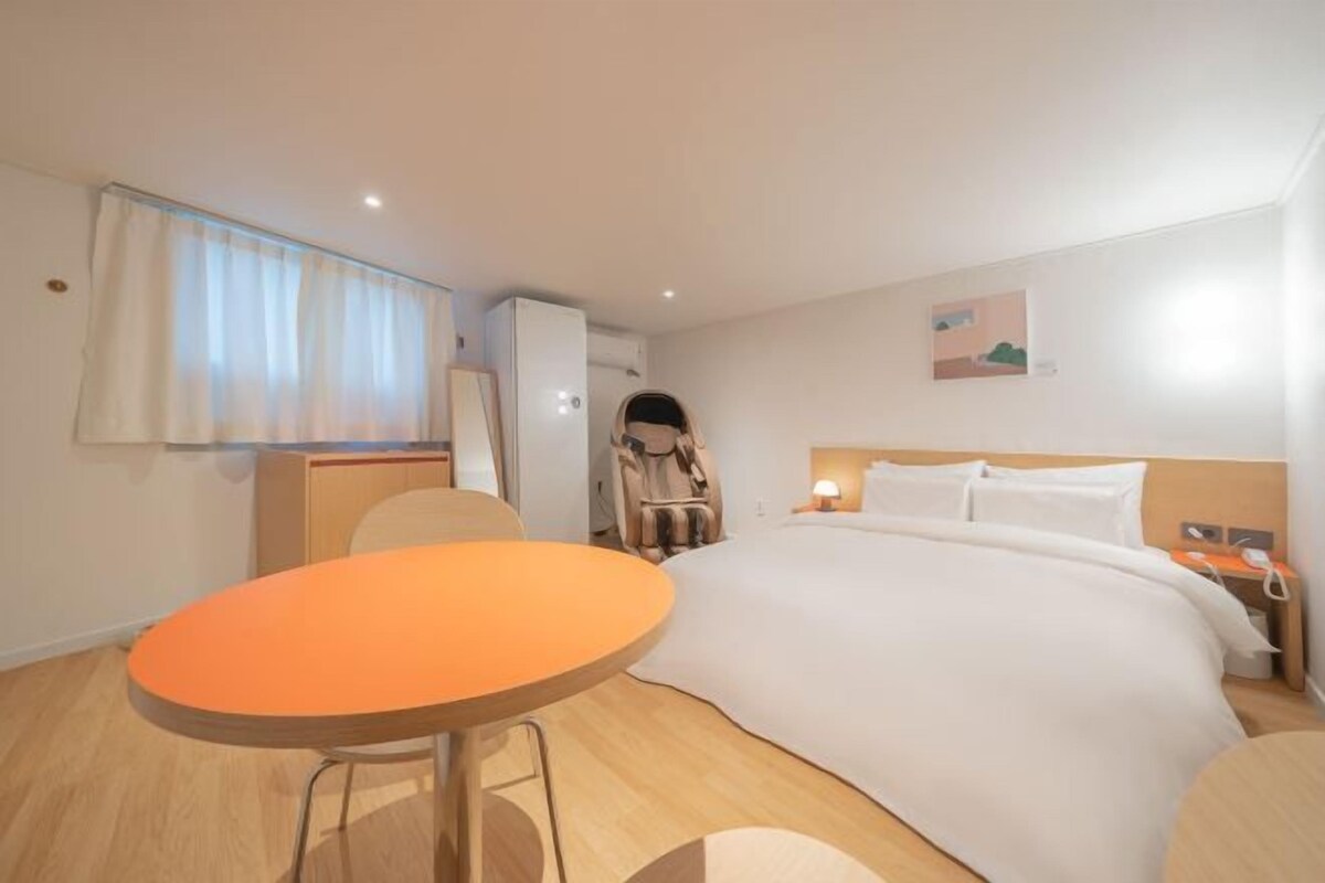 Habitación de hotel con cama, una mesa, una silla, escritorio, lámpara y un cuadro en la pared.
