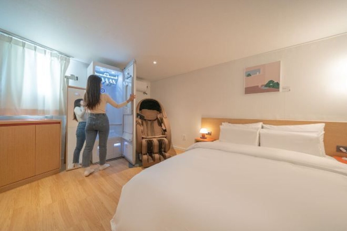 Une chambre d’hôtel équipée d’un lit, d’un fauteuil massant, d’un bureau et d’une fenêtre avec des rideaux.