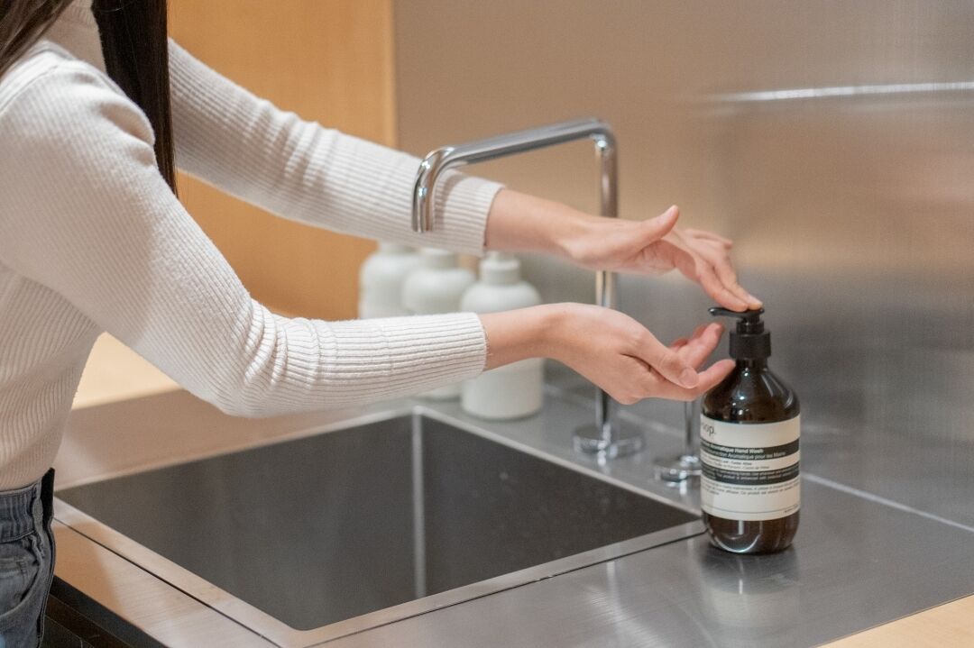 A person using a soap dispenser at a sink.