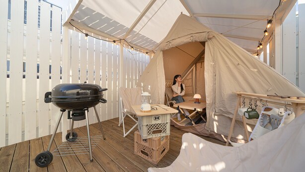 Ein überdachter Außenbereich mit Grill, Tisch mit Laterne und einer Hängematte.