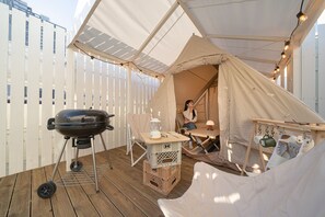 Ein überdachter Außenbereich mit Grill, Tisch mit Laterne und einer Hängematte.