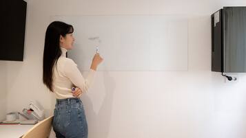 A person standing in front of a whiteboard in a room with a desk and a black cabinet.