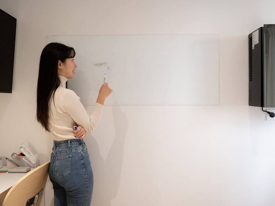 A person standing in front of a whiteboard in a room with a desk and a black cabinet.