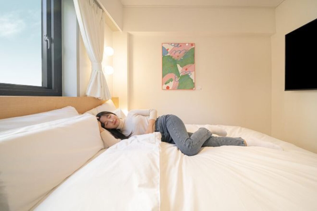 Une chambre d’hôtel avec un lit, une fenêtre avec des rideaux et un téléviseur fixé au mur.