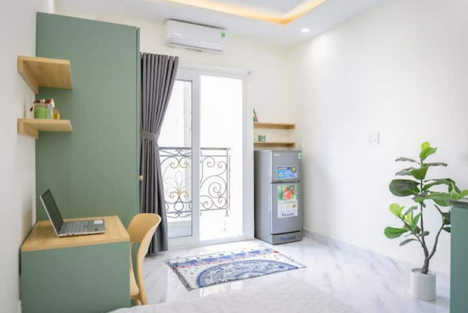 Una sala de estar moderna con una laptop sobre una mesa de madera, un sofá, un refrigerador y una planta en maceta.