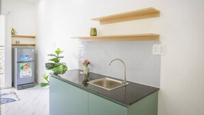 A modern kitchen with a built-in sink, a refrigerator, and a small potted plant. - 2/studio Neuf, Confortable et Coloré Avec Balcon (Ho Chi Minh City)