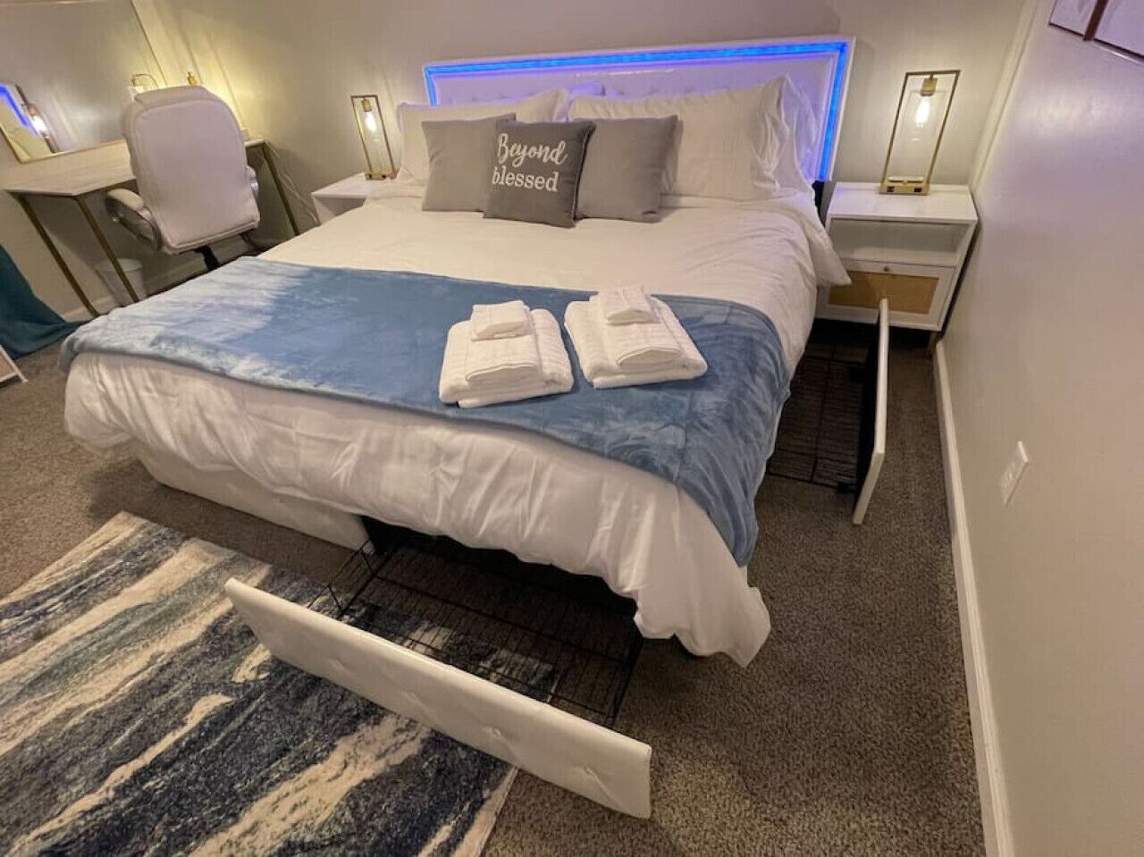 Een net opgemaakt bed met een blauw-witte dekbedovertrek, twee gevouwen handdoeken en een kussen met de tekst 'Beyond blessed'.