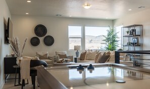 A modern living room with a pool table, a sofa set, and a large window offering a view of the desert.