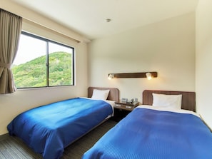 Une chambre dâhĂŽtel avec deux lits, une fenĂȘtre avec des rideaux, une table de chevet avec une lampe et une vue sur la verdure.