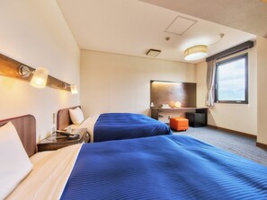 Een hotelkamer met twee bedden, een bureau, een stoel, een lamp, een raam en uitzicht op de omgeving.