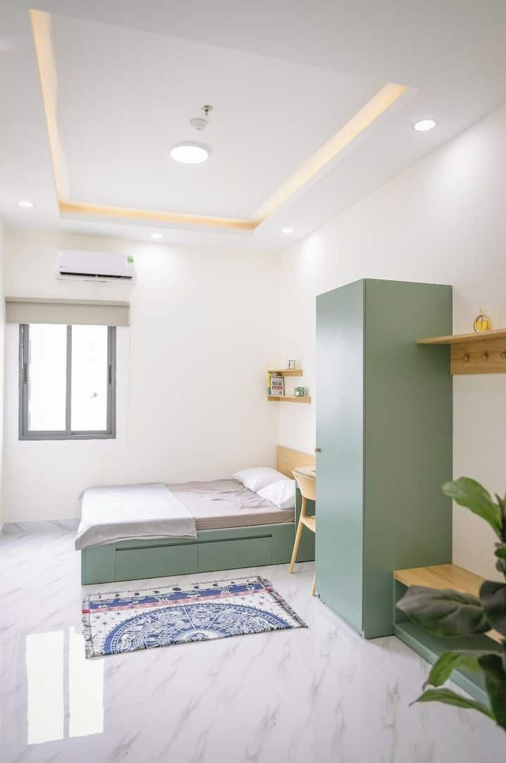 Une chambre moderne avec un lit, un bureau, une armoire verte et une fenêtre.