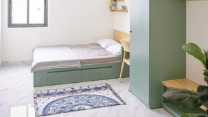 Een moderne slaapkamer met een bed, een bureau, een groene kledingkast en een raam.