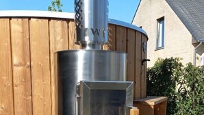 Una estufa de leña con chimenea, una terraza de madera y una casa al fondo.