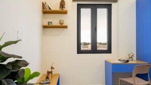 Ein Zimmer mit Schreibtisch, Stuhl, einem Fenster mit Blick und Regalen mit Büchern und einer kleinen Pflanze.