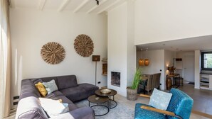 A modern living room with a grey sectional sofa, a blue armchair, and a coffee table. There are two wall art pieces and a fireplace. - Holiday Home by the Sea and Dunes (Nieuwvliet-Bad)