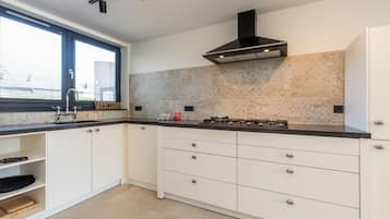 Een moderne keuken met witte kasten, een zwart aanrecht, een gasfornuis en een raam met jaloezieën.