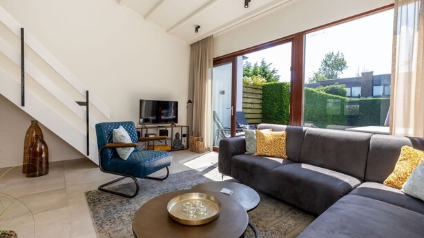 A modern living room with a sofa, a chair, a coffee table, and a TV. - Holiday Home by the Sea and Dunes (Nieuwvliet-Bad)