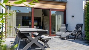 A patio with a table and chairs, a sliding glass door, and a small outdoor seating area with lounge chairs. - Holiday Home by the Sea and Dunes (Nieuwvliet-Bad)