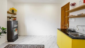 Eine kleine Küche mit Kühlschrank, gelben Schränken und einem Marmorboden.