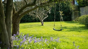 A garden with a swing set, a tree, and purple flowers.