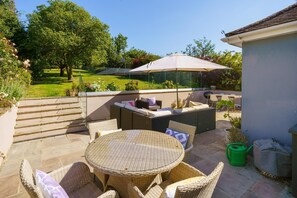 Un patio al aire libre con mobiliario de mimbre, una mesa redonda y un paraguas grande.