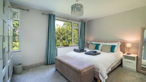 A bedroom with a large bed, a bedside table, a bench, a window with curtains, and a hanging light fixture.