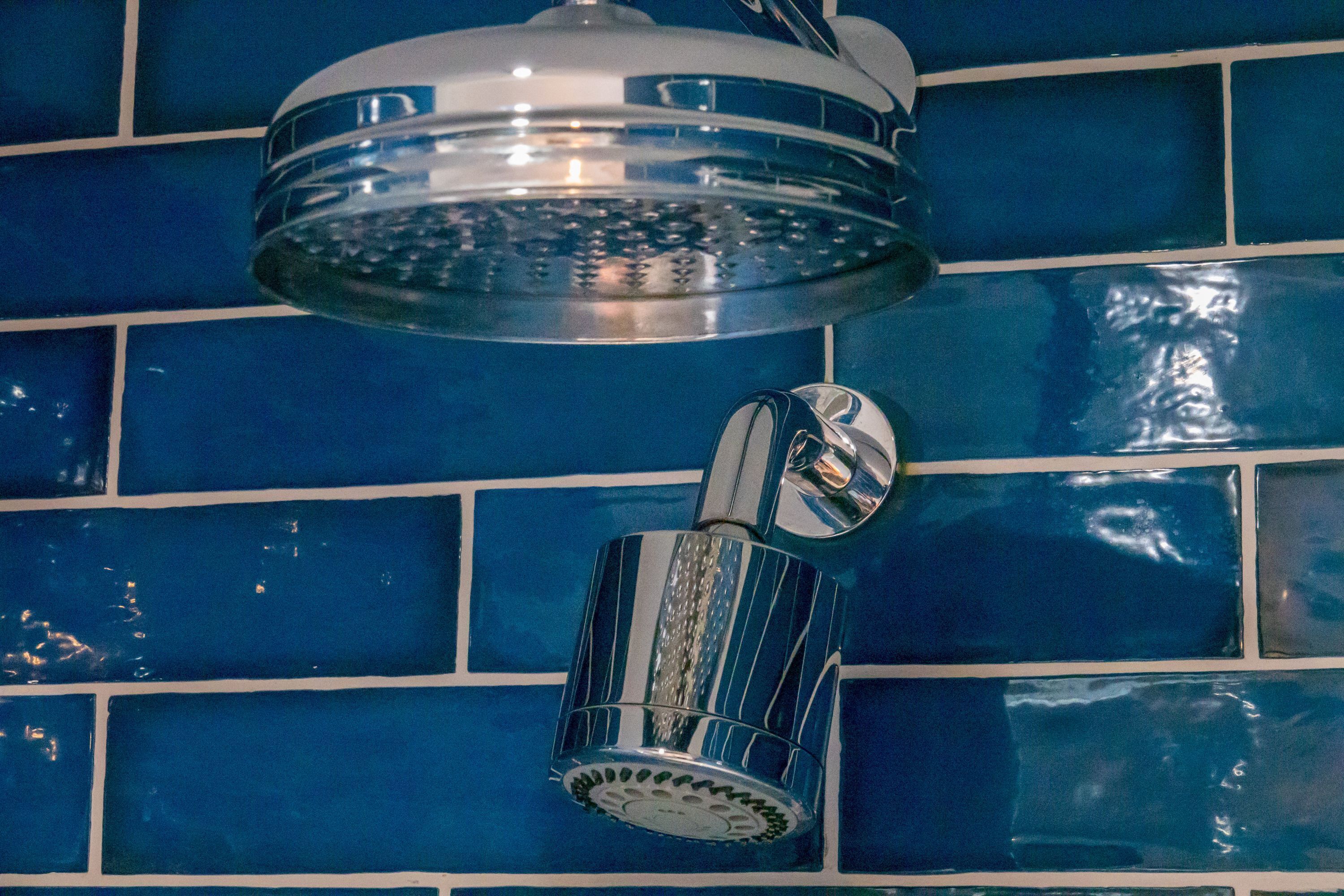 Un baño con pared de azulejos azules y ducha con cabezal cromado.