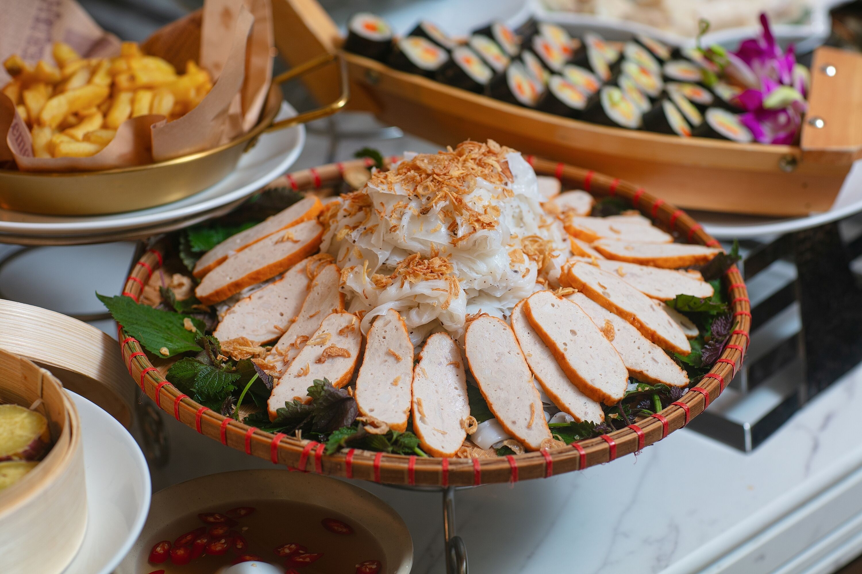 Un bufé con diversos platillos, entre ellos carne en rodajas, comida frita y sushi.
