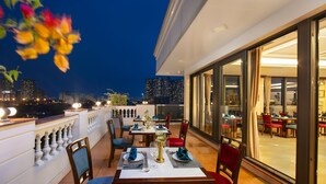 An outdoor dining area with tables set for two, featuring a city skyline view in the background. - Gloud Hotel (Hanoi)