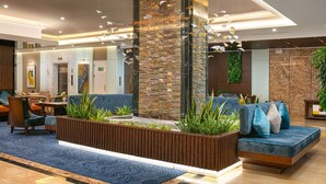 A modern lobby with a reception desk, seating area, and a decorative wall with hanging elements. - Gloud Hotel (Hanoi)