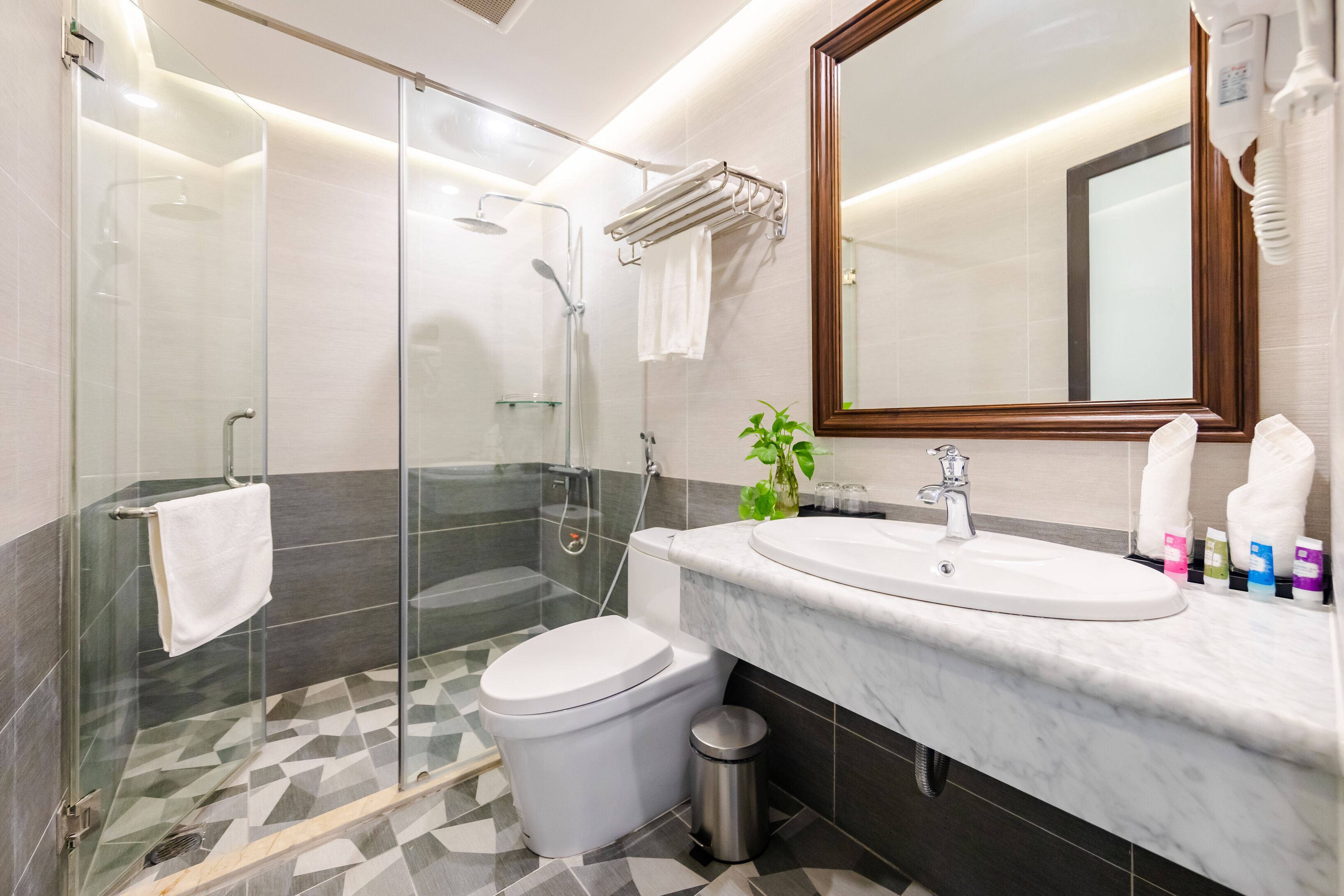Une salle de bain moderne avec une douche à parois de verre, des toilettes blanches, un lavabo en marbre et un grand miroir.