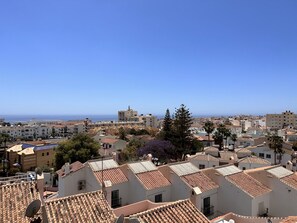 Un pueblo costero con edificios de tejas color terracota, una torre destacada y un cielo azul despejado.