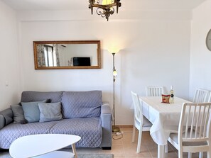 A living room with a grey sofa, a white table, and a dining area with white chairs. - Capri Sunset by Casasol (Nerja)