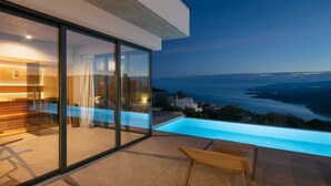 A modern outdoor living area with a glass wall, a pool, and a view of the sea.