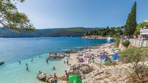A coastal beach with clear waters, rocky terrain, and people swimming and sunbathing.