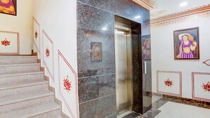 Un escalier orné de panneaux décoratifs, un mur en marbre et un ascenseur.