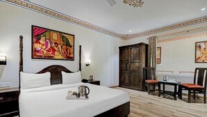 Une chambre d’hôtel avec un grand lit, une armoire en bois, un bureau avec une chaise et deux tableaux accrochés aux murs.