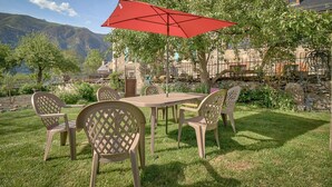 Un patio con una mesa y sillas, un paraguas rojo y una pared de piedra con vistas a las montañas.