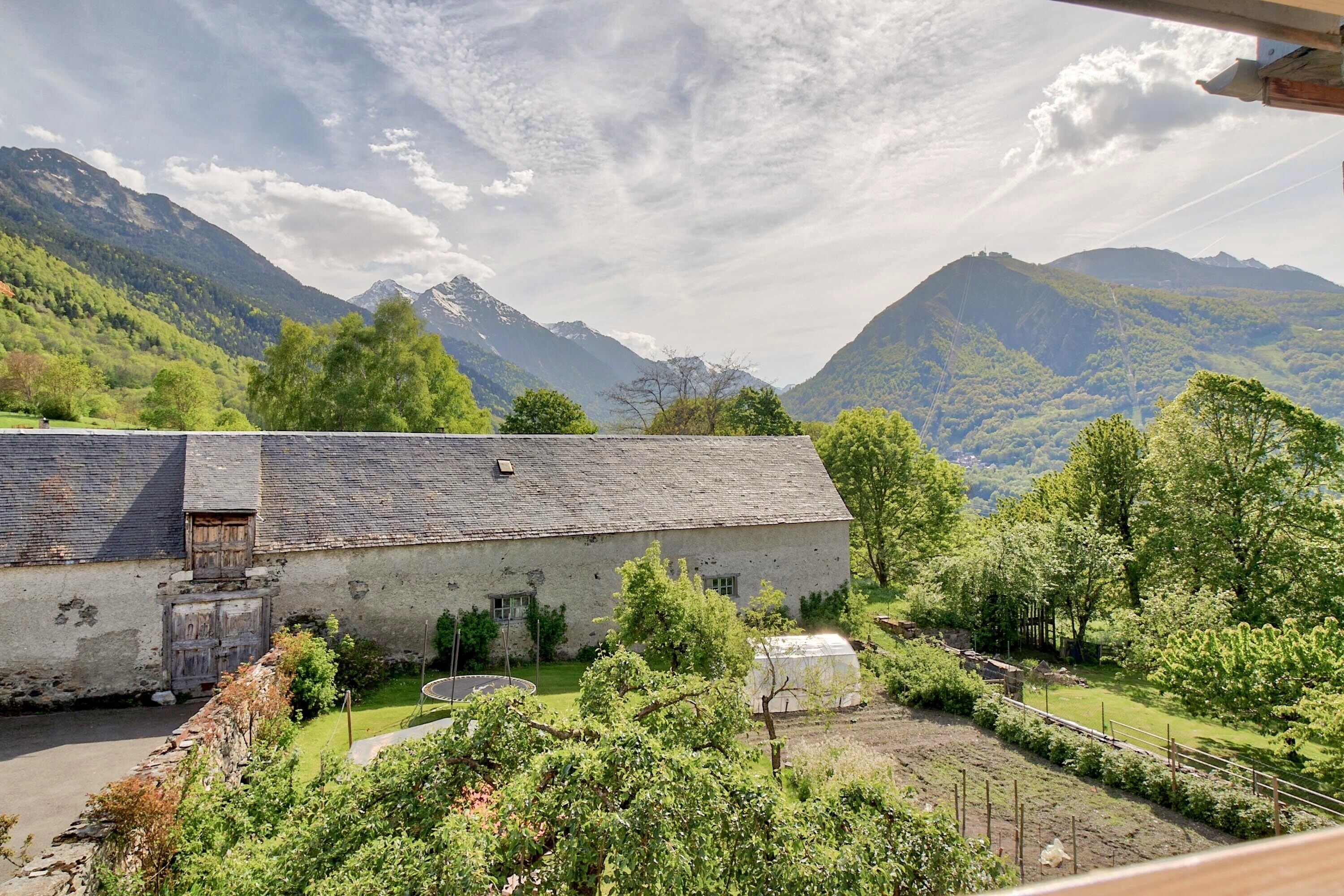 A rustic building with a sloped roof, surrounded by lush greenery and mountains in the background.