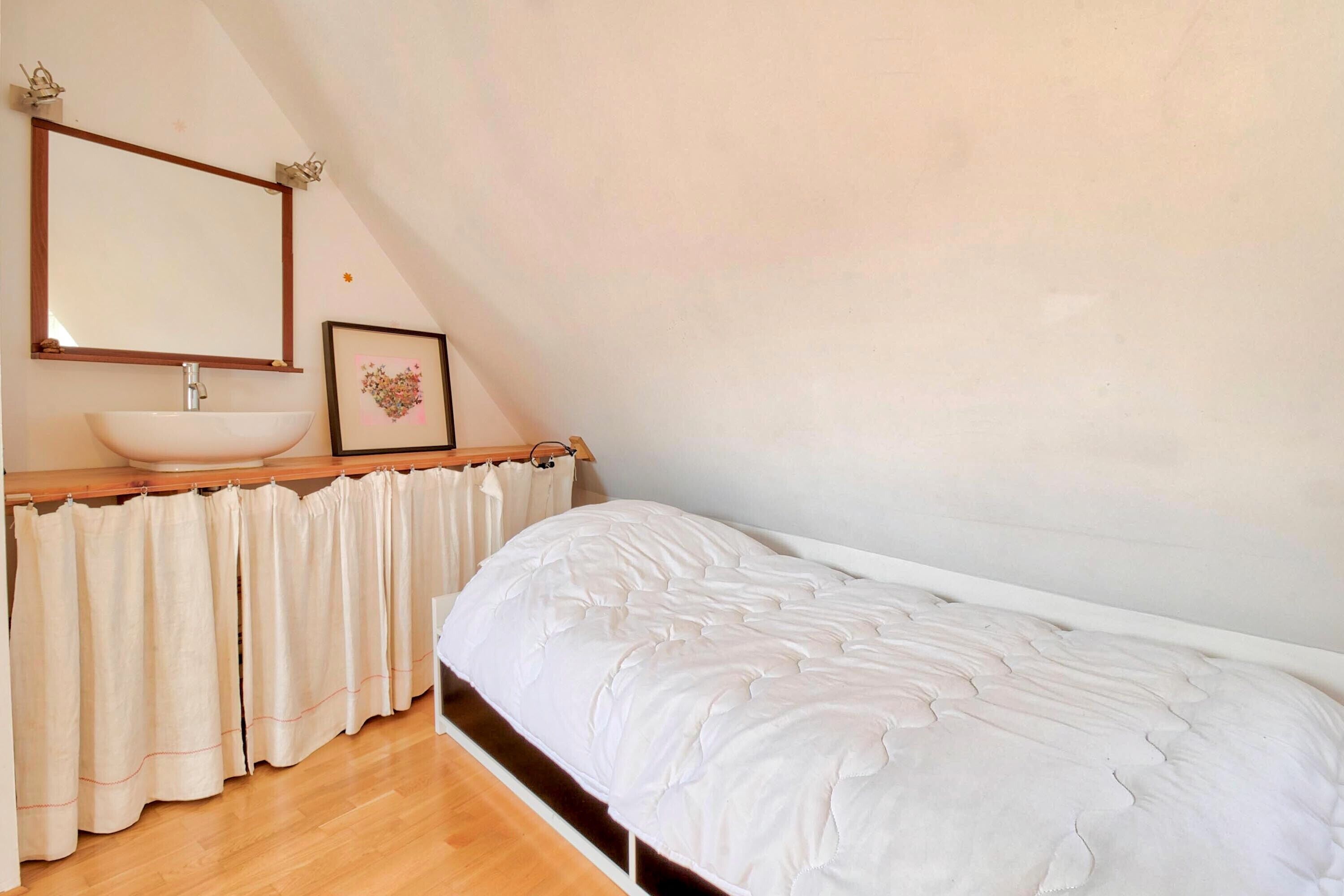 Ein Schlafzimmer mit einem Einzelbett, einem Nachttisch, einem Spiegel, einem Waschbecken und einem gerahmten Bild an der Wand.