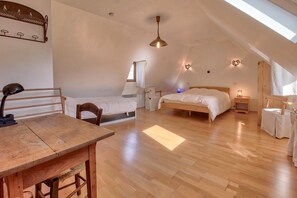 Une chambre avec un plafond en pente, une table en bois, deux lits, un luminaire suspendu et une étagère fixée au mur.