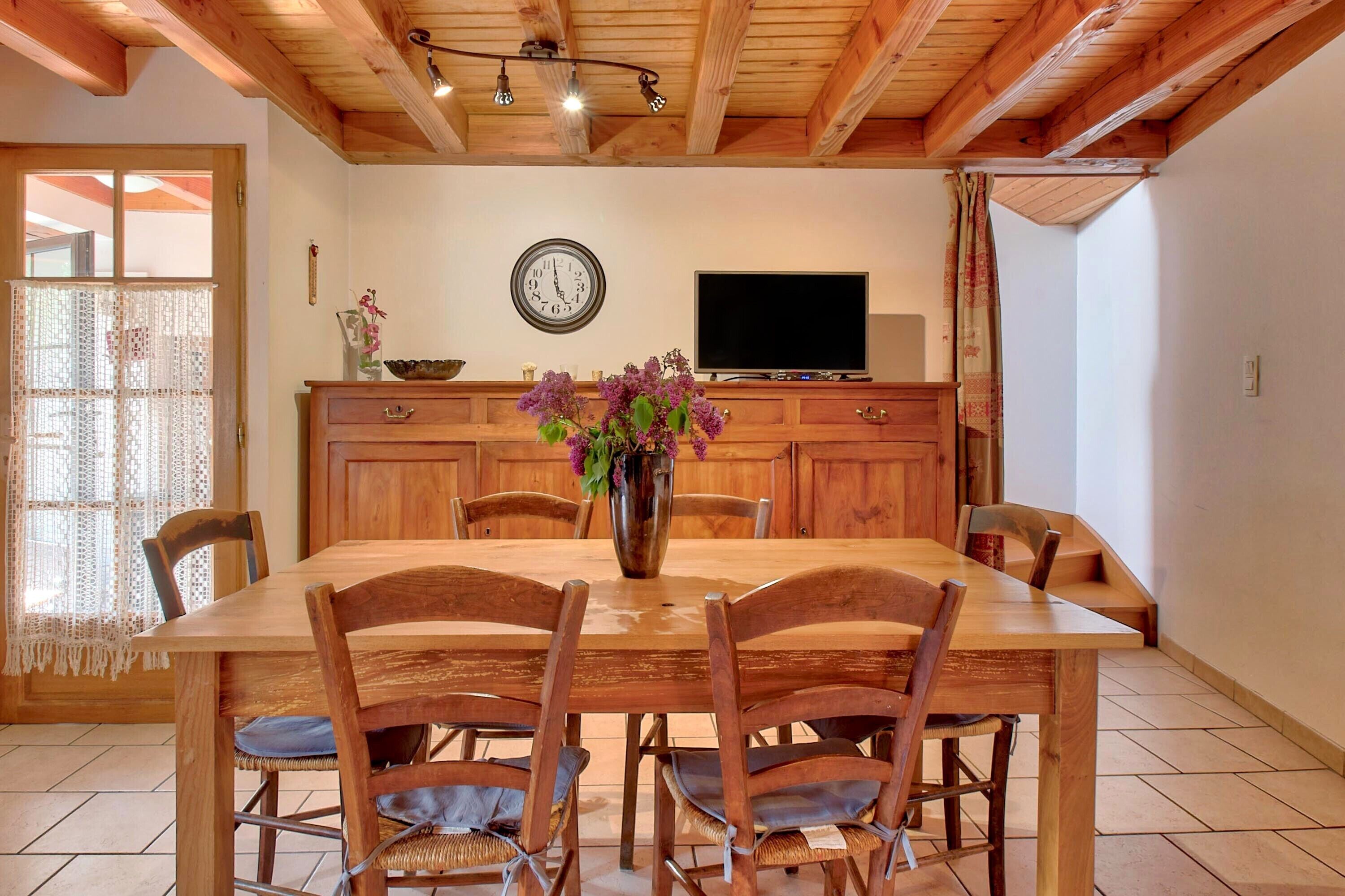 Ein Holztisch mit Stühlen, eine Vase mit Blumen, eine Uhr und ein Fernseher auf einer Holzkommode.