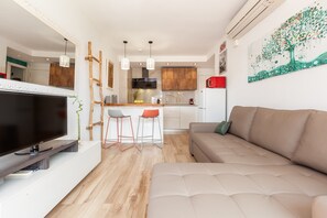 A modern living room with a flat-screen TV, a sofa, and a dining area with stools.