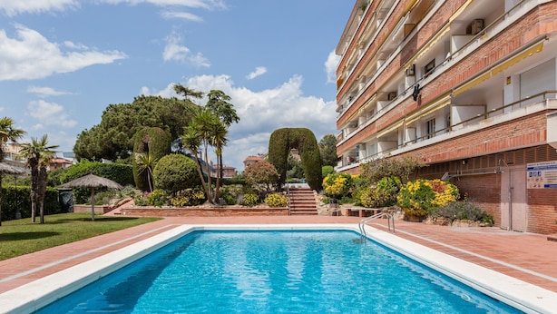 Une piscine entourée d’un bâtiment en briques doté de balcons, d’arbres et surplombant un ciel dégagé.