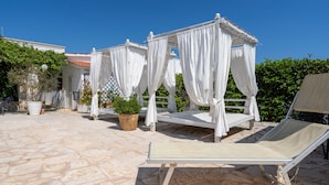 Un patio de piedra con un toldo blanco y una silla de descanso.
