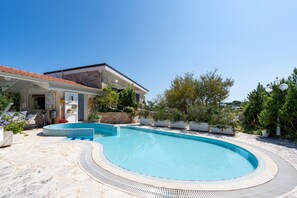 Ein Pool mit gewölbter Kante, eine Steinterrasse und ein Gebäude mit einem Ziegeldach.