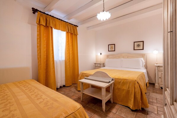 Un dormitorio con cama, mesitas de noche, una silla y una ventana con cortinas.
