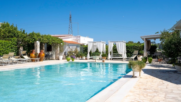Una piscina con sillas de descanso, plantas en macetas y una pérgola con cortinas blancas.