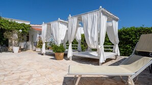 A stone patio with a white canopy and a lounge chair.