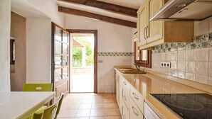 A kitchen with a dining area, a stove, cabinets, and a view through an open door. - Country House 'Cadernera' with Private Pool, Wi-Fi and Air Conditioning (Búger)